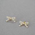 Detalle de elegantes pendientes de lazo con perlas tejidas y detalles dorados sobre gris - Stud aretes