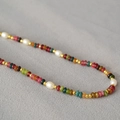 Detail of colorful beads and pearls necklace with gold spacers on grey fabric - Tourmaline Color