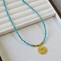 Blue apatite beaded necklace with a golden evil eye coin pendant on a white jewelry display - Colorful Zirconia