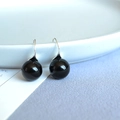 Macro detail of glossy black agate sphere earrings hanging on a white ceramic plate edge - 12mm