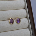 Vista macro di orecchini a perno ovali in pietra naturale viola con castone dorato in argento - Ametista