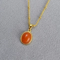 Detailed macro view of an oval orange gemstone pendant on a gold beaded chain necklace - Orange Aventurine