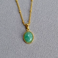 Macro view of a gold bead chain with an oval green stone pendant on textured fabric - Amazonite