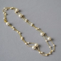 Dettaglio di una lunga collana dorata a due strati con perle bianche su tessuto grigio - Catena per Maglione Lunga