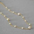 Dettaglio ravvicinato di perle tonde lucide su una collana lunga a catena dorata sottile - Collana girocollo corta