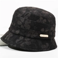 Close-up of black floral fabric texture and golden metal logo on the baker boy hat - One Size 58cm / Bucket Hat Black