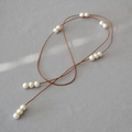 Collana lunga con perle minimalista e cordino in pelle marrone su fondo grigio - Corda in pelle marrone