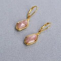 Vista macro de pendientes de palanca con piedras semipreciosas rosas y engaste dorado - Estilo Rodocrosita