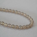 Macro shot of translucent smoky gray agate beads on a textured light gray fabric - 8mm