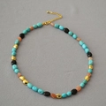 Collana barocca con perline turchesi e tocchi dorati su sfondo tessile grigio - Collana