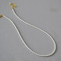 Elegante collana di perle bianche con chiusura dorata e catena regolabile su fondo grigio - Piccola Perla di Riso 3*5mm