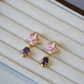 Dettaglio di orecchini dorati con petali in smalto rosa e zircone viola ovale - Stile Fiore Rosa Strass Viola