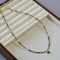 Détail du collier de perles noires et dorées avec pendentif carré dans un présentoir - Noir & Or
