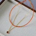 Detail showing double-layered gold necklace with orange beads and red square gemstone pendant - Layered Style