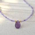 Macro shot of purple teardrop gemstone pendant with faceted beads on fabric - Amethyst