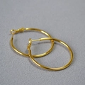 Minimalistische goldfarbene C-förmige Creolen mit glatt polierter Oberfläche auf grauem Grund - Gold 4cm