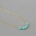 Detail of minimalist gold bead chain with faceted turquoise beads on a grey background - Smiley Face