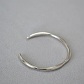 Bracciale aperto argento minimalista con linee ondulate su sfondo grigio - Oro Bianco