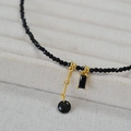 Elegante collana di perline con spinello nero e ciondolo dorato su vassoio beige - Nero