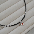 Primer plano de collar de cuentas negras con colgante de plata y gema naranja - Rojo Anaranjado