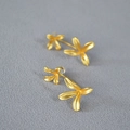 Vista macro de pendientes de flores en oro mate con dos flores de cuatro pétalos sobre tela - Chapado en oro