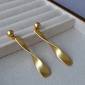 Pendientes largos minimalistas en oro mate con metal retorcido sobre joyero - Dorado