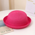 Détail d'un chapeau de soleil rose en paille tressée avec bord incurvé sur fond blanc - Style Enfant / Rouge Rose