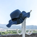 Navy blue woven straw sun hat with large black bow tie hanging on a white rack - M (56-58cm) / Navy Blue