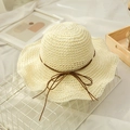 Close-up of hand-woven straw beach hat with wavy brim and brown ribbon bow detail - M (56-58cm) / Cream