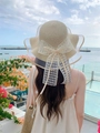 Close-up of wavy brim straw hat with lace bow and mesh trim against beach background - M (56-58cm) / Beige