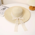 Detalle de un sombrero de paja de ala ancha con lazo de encaje blanco sobre la mesa - M / Beige