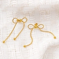 Detalle de pendientes de lazo dorado con textura de cadena de serpiente sobre tela blanca - Dorado