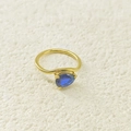 Détail macro d'une bague goutte dorée avec zircon bleu taille poire sur fond de textile blanc - Septembre Bleu Roi (Couleur Saphir)