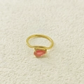 Gros plan d'une pierre précieuse rose en forme de poire sur une bague dorée en acier - Juillet Rose Rouge