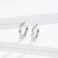 Orecchini a cerchio cavo a forma di C in argento lucido su sfondo minimalista bianco - Argento 925 / Oro Bianco