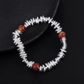Macro detail of beaded silver bracelet with red agate accents on natural black stone plate - Orange Style