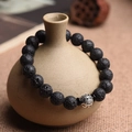 Dettaglio di perline in pietra vulcanica e ciondolo argento su bracciale elastico - Stile Pixiu