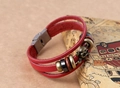 Dettaglio del bracciale in pelle rossa intrecciata con teschi in bronzo e chiusura in metallo - Rosso