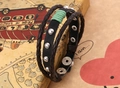 Dettaglio di un bracciale punk multistrato in pelle con rivetti argento e cordino verde - Nero