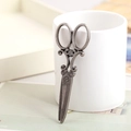 Vintage silver alloy scissor pendant with scroll handle leaning on white ceramic cup - Antique Silver