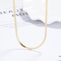 Elegante goldene flache Schlangenkette auf weißem Tablett mit Modezeitschriften-Stil - 925er Silber / Gold