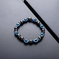 Handmade hematite bead bracelet featuring blue evil eye charms on a dark leather surface - Evil Eye Style (S745-A)