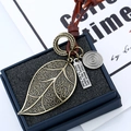 Détail du pendentif feuille en bronze vintage et charme gravé sur un cordon en cuir marron - Grande Feuille