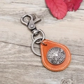 Retro brown leather keychain with silver dragon emblem on a light wooden background - Tan