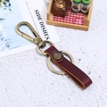 Vintage Bronze Schlüsselanhänger mit dunkelrotem Lederband auf eleganter Steinfläche - Braun