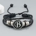 Detalle de pulsera de cuero negro multicapa con dije de letra B y cuerda trenzada negra - Letra B