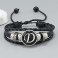 Detalle de pulsera multicapa de cuero con cordones trenzados y dije con la letra D - Letra D