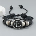 Detail of layered black leather bracelet featuring letter E glass dome and metallic beads - Letter E
