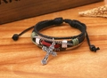Dettaglio del bracciale multistrato in pelle con ciondolo a croce su fondo di legno - Nero
