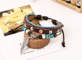 Dettaglio di un bracciale multistrato in pelle intrecciata retrò con ciondolo ala e perline - Marrone
